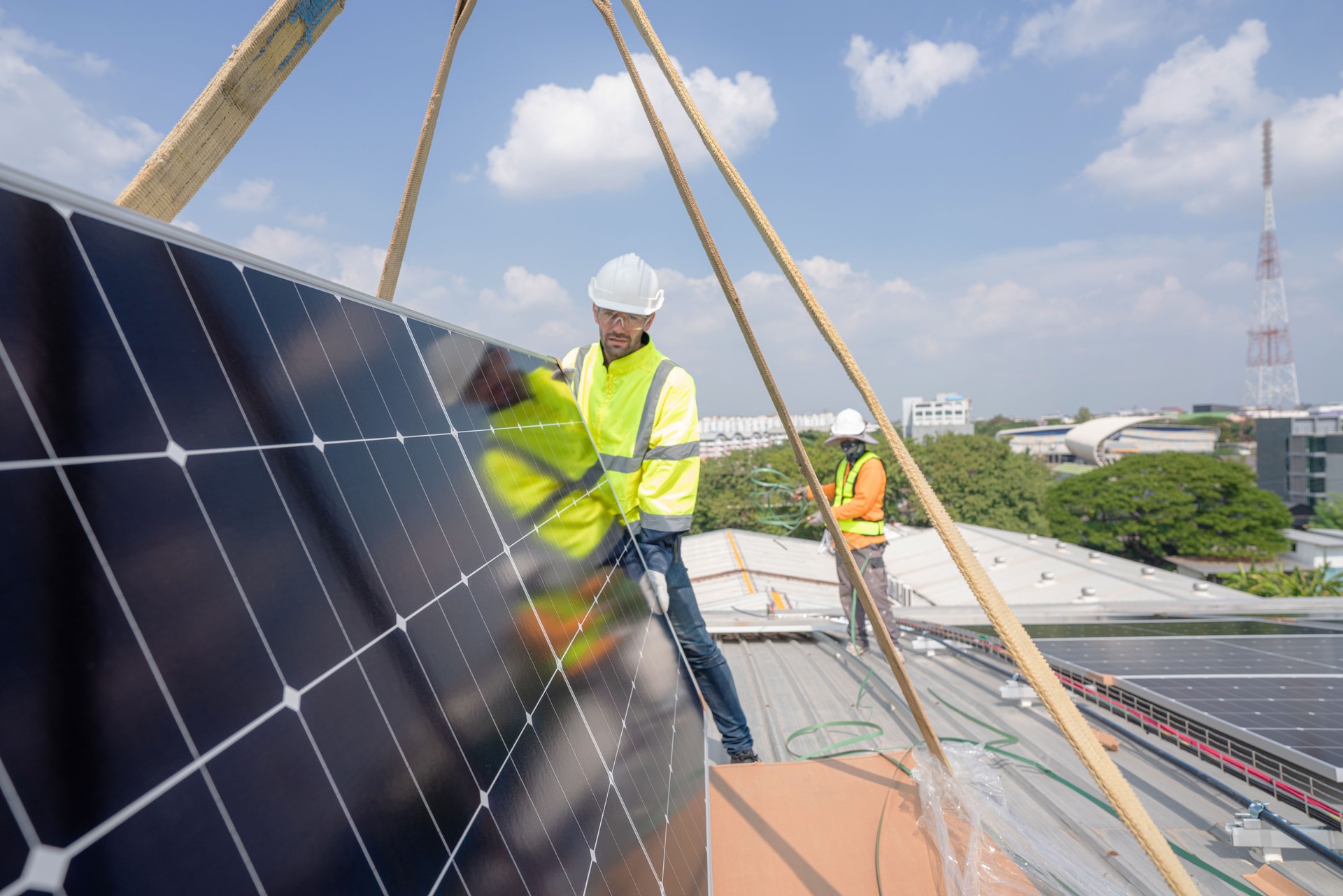 Men technicians carrying photovoltaic solar moduls on roof.